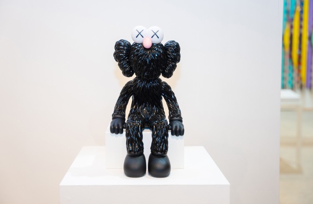 A black bff KAWS figure, Seeing Black (BFF Lamp), 2020, sits on display.