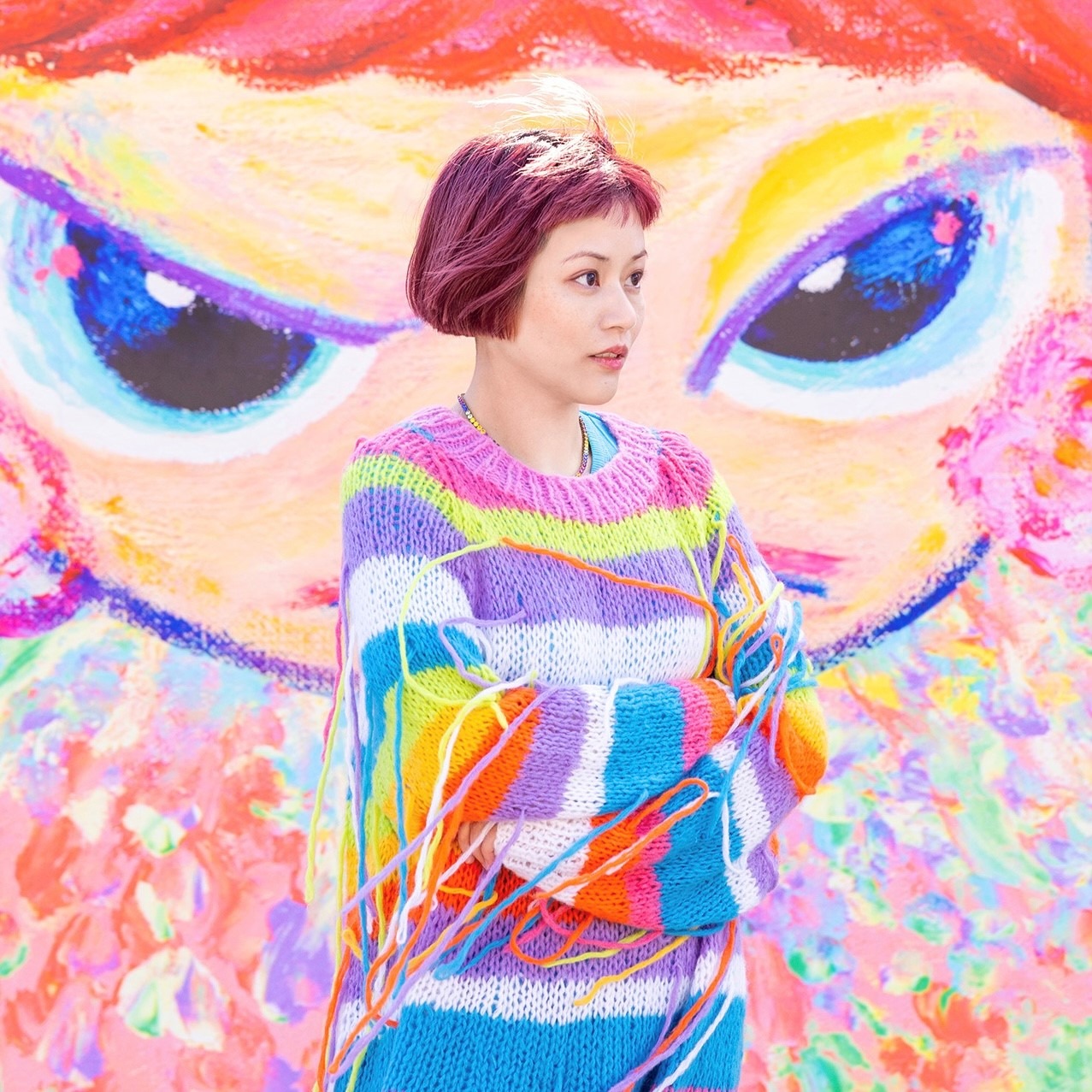 Bringing together a group of powerful women, art exhibit HER features artist, Bibi Lei, who stands in front of her painting &lsquo;Flourishing Girls,&rsquo; wearing a sweater to match.
